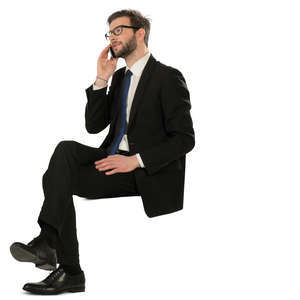 man in a black suit sitting and talking on a phone