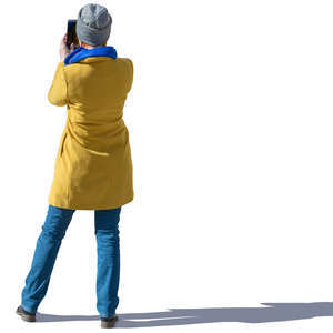 woman in a yellow autumn coat standing and taking a picture