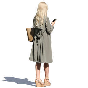 woman in a light trenchcoat standing and texting