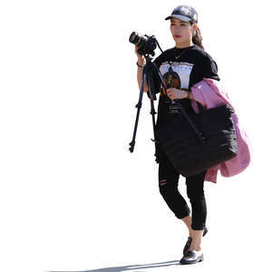 backlit asian woman walking and carrying a camera and tripod