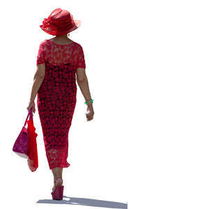 backlit woman in a red dress and hat walking