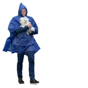 man wearing a blue hooded rain jacket walking and  carrying a small dog