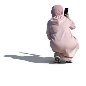 woman wearin g a pink abaya and hijab squatting and taking a picture