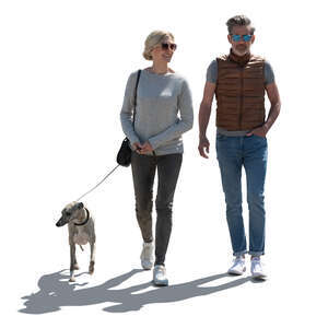 backlit man and woman walking a dog