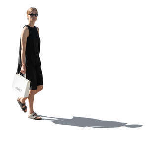 backlit woman in a black dress carrying a shopping bag walking