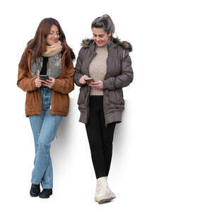 two women leaning against the wall and looking at their phones