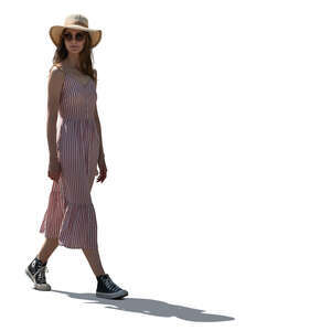 backlit young woman in a dress and wearing a hat walking