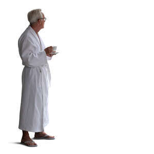 cut out older man in a white bathrobe standing by the window and drinking coffee