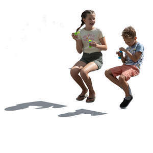 two backlit children sitting and blowing soap bubbles