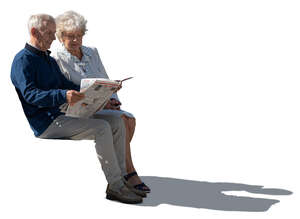 sidelit elderly couple sitting and reading a newspaper