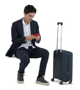 man in a suit and with a travel bag sitting and checking his phone 