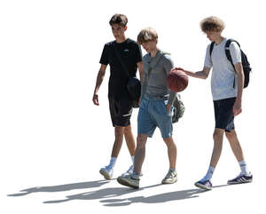 three backlit teenage boys with a basketball walking