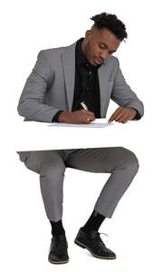 black man in a grey suit sitting and writing