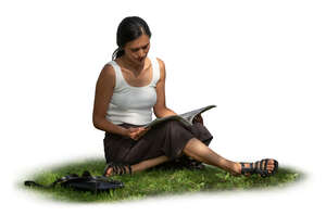 woman sitting on the grass in the partial shade and reading a magazine