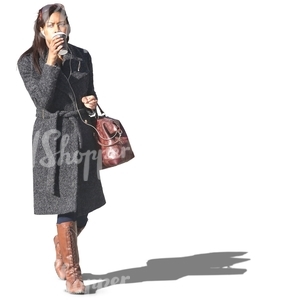 black woman in a grey coat walking and drinking coffee