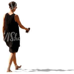 woman in a black summer dress walking barefoot on the beach