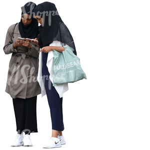 two young muslim women standing and looking at their phones