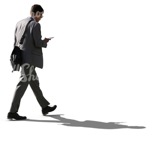backlit businessman walking while looking at his phone