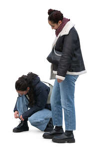 woman tying her shoe laces and her friend standing and waiting