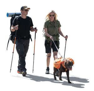 two cut out backlit people with trekking poles and a dog hiking