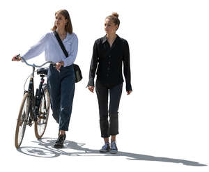 two backlit women with a bike walking