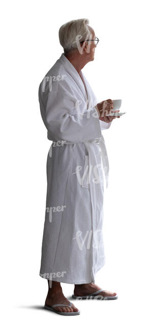 cut out older man in a white bathrobe standing by the window and drinking coffee