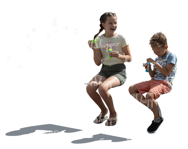 two backlit children sitting and blowing soap bubbles