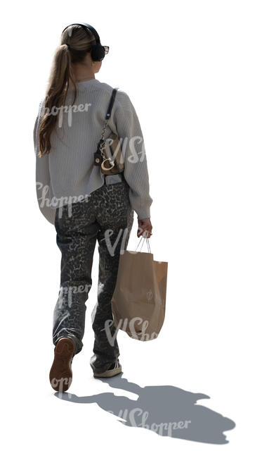 backlit woman with headphones and a groceries bag walking